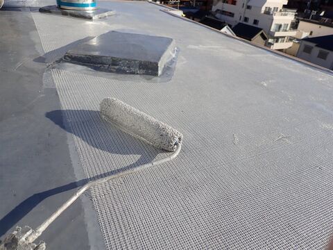 屋上の床にメッシュを敷き、ローラーで防水の材料を塗る途中(イメージ)