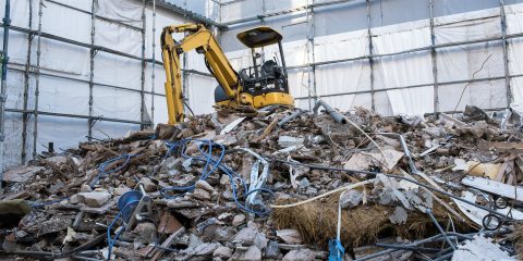 養生シートに囲まれた解体現場の瓦礫と小型の油圧ショベル(イメージ)