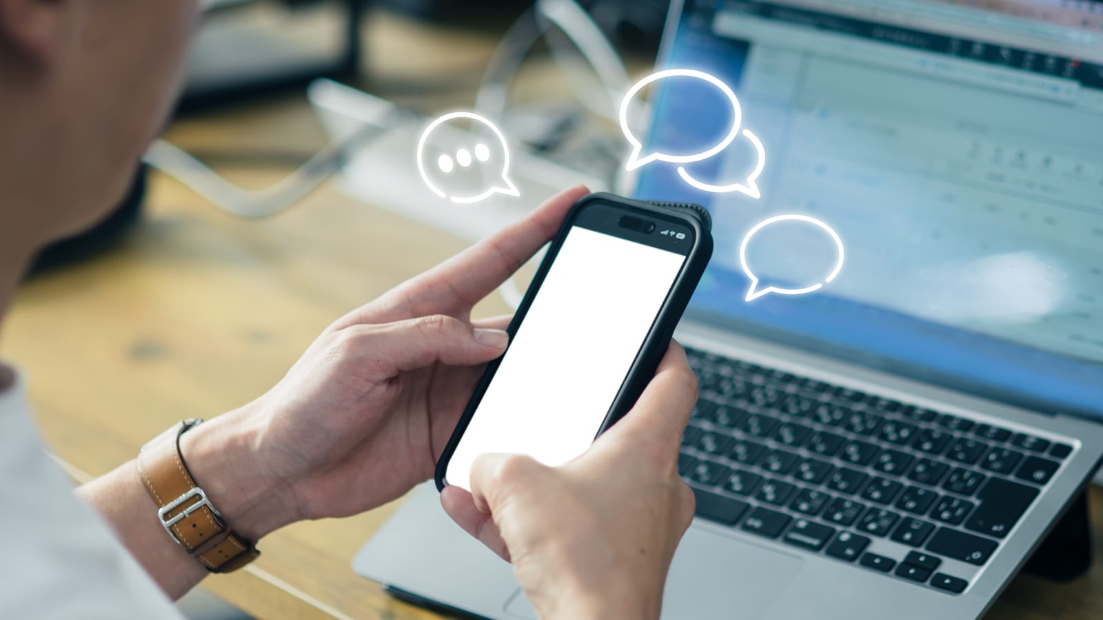 ノートパソコンの前でスマートフォンを両手で持ち、入力している手元