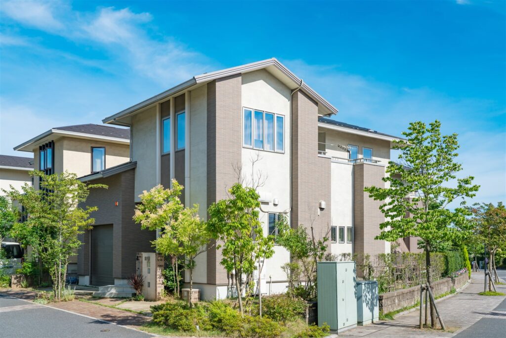 茶色と白の外壁の新しい二階建ての一戸建て。前に植え込みと歩道がある