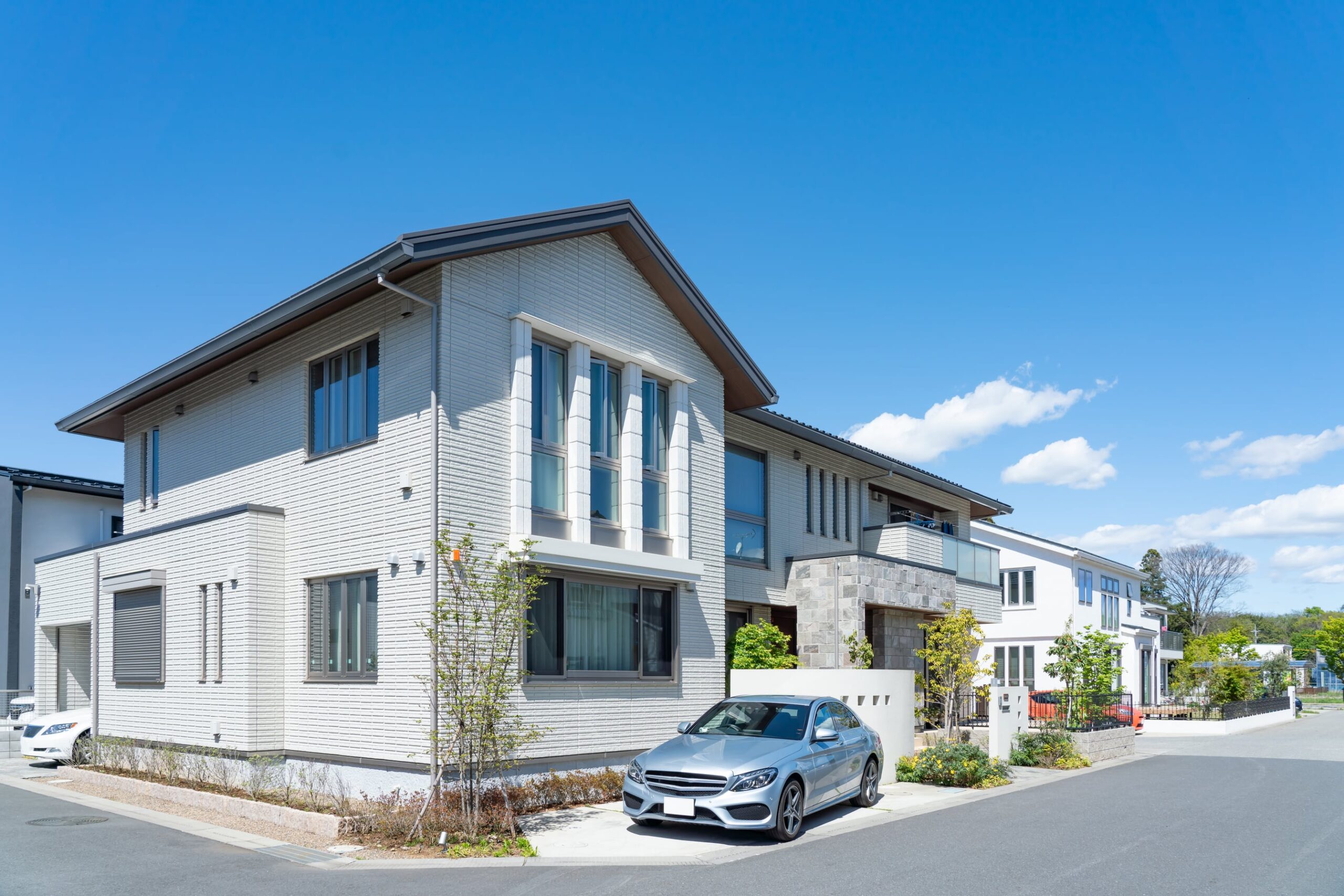 白い外壁の2階建ての家と、前に停めた車
